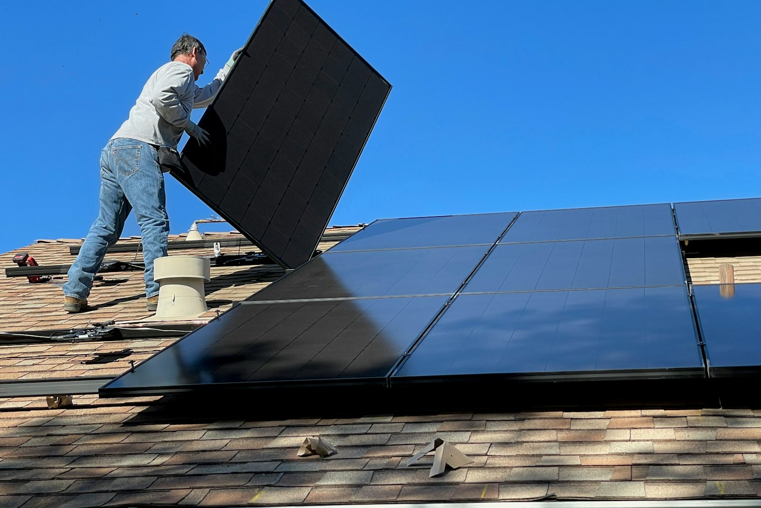 Installateur tilt een zwart zonnepaneel met de achterkant naar voren boven een dak met dakpannen